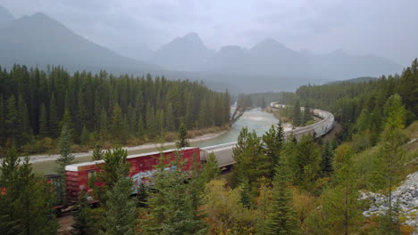 Moving-train-with-mountain-scenery-pulling-rail-road-cars-through-Morant's-curve---Alberta,-Canada