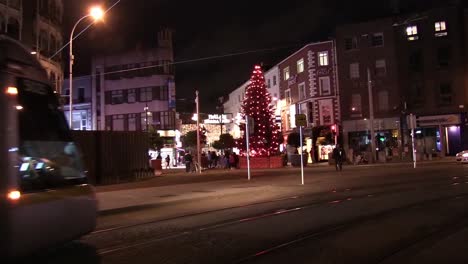 Foto-Fija-Del-Tranvía-Luas-Pasando-Y-El-árbol-De-Navidad-En-Graton-St-Con-Gente-Reunida-A-Su-Alrededor