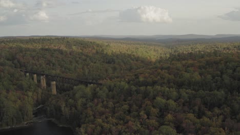 Railroad-Trestle-crossing-the-outlet-of-a-lake-with-early-fall-foliage-at-sunset-AERIAL-ORBIT