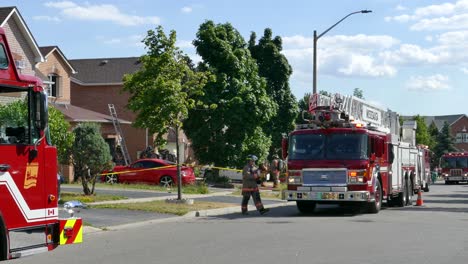 Dos-Camiones-De-Bomberos-Estacionados-En-La-Escena-Del-Incendio,-Bombero-Cerrando-El-área-Con-Cinta-De-Emergencia