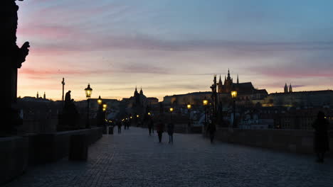 Dunkelheit-Und-Silhouetten-Von-Menschen-Auf-Der-Karlsbrücke,-Prag-Tschechische-Republik-Mit-Burg-Auf-Hügel-Unter-Sonnenuntergangshimmel-Während-Der-Covid-19-viruspandemie,-Zeitlupe