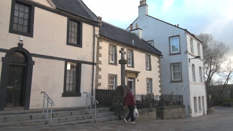 Slow-motion-of-a-man-walking-past-the-wooden-Mercat-Cross-with-17th-and-18th-century-buildings