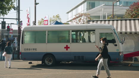 Menschen-In-Gesichtsmaske,-Die-An-Einem-Blutmobil-Vorbeikommen,-Das-Während-Des-Covid-19-ausbruchs-In-Tokio,-Japan,-Auf-Der-Blutspendestation-Des-Roten-Kreuzes-Auf-Der-Straße-Von-Tokio-Geparkt-Wurde