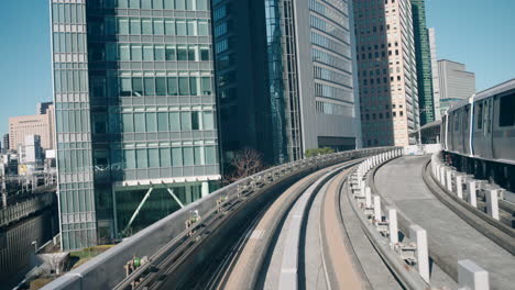 Un-Punto-De-Vista-De-Un-Monorraíl-Yurikamome-Que-Llega-A-Una-Estación-Con-Rascacielos-En-El-Fondo-En-Tokio,-Japón