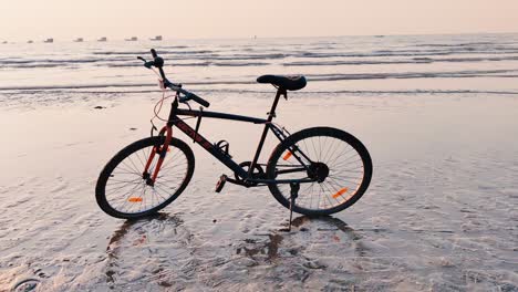 Fahrrad-An-Der-Strandküste-Geparkt-Mit-Reflexion-Im-Wasser-Während-Des-Videohintergrunds-Der-Sonnenuntergangszeit-In-4k-Auflösung