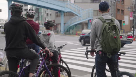 Cyclists-Wait-For-Green-Signal-At-City-Crosswalk-During-Daytime-In-Tokyo,-Japan