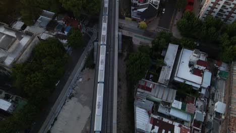 Tilt-up-of-train-leaving-station-revealing-Belgrano-neighborhood-buildings-at-sunset,-Buenos-Aires,-Argentina