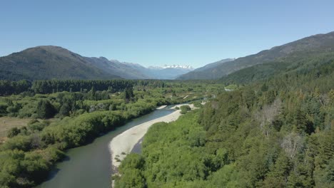 Aerial-dolly-in-of-Rio-Azul-stream-between-pine-tree-woods-with-mountains-in-background,-Patagonia-Argentina