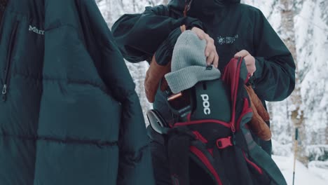 Mann-Bereitet-Tasche-Mit-Skiausrüstung-Und-Skihelm-Vor,-Bevor-Er-Skifahren-Geht,-Während-Er-In-Einem-Verschneiten-Wald-Steht,-Der-Mit-Bäumen-Bedeckt-Ist