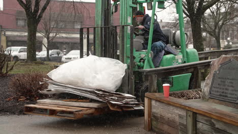 Forklift-operator-beginning-to-back-through-narrow-walkway-outdoors-with-trash-in-falling-snow,-Slot-Motion