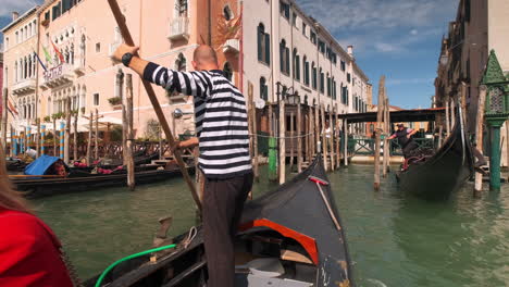 Italian-Gondolier-rowing-gondola-and-docking-at-pier-during-sunny-day-in-Venice