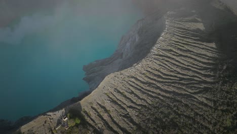 Scenic-shot-of-Ijen-stratovolcano-turning-towards-cliff-ridge-with-stunning-blue-acidic-lake
