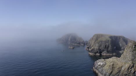 Seashore-aerial-flies-into-afternoon-fog-on-jagged-ocean-rock-islets