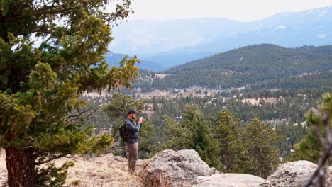Solo-male-hiker-standing-on-a-windy-viewpoint-and-looking-through-a-monocular-or-binoculars-at-something-in-the-distance
