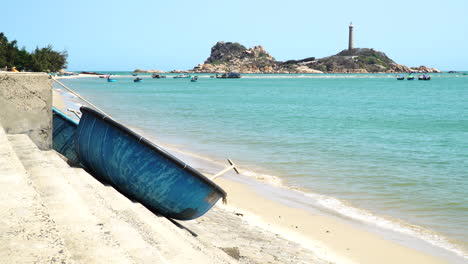 Barcos-Coracle-Amarrados-En-La-Playa-Vietnamita,-Faro-Ke-Ga-En-Segundo-Plano