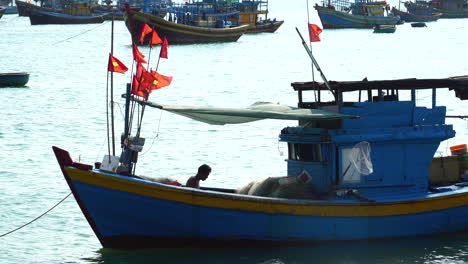 Silhouette-Des-Fischers-Auf-Dem-Befestigungsnetz-Des-Bootes,-Flaggen-Vietnams-Im-Wind