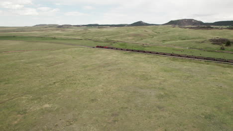 Aerial-approach-towards-end-of-long-coal-train-moving-through-open-farmland