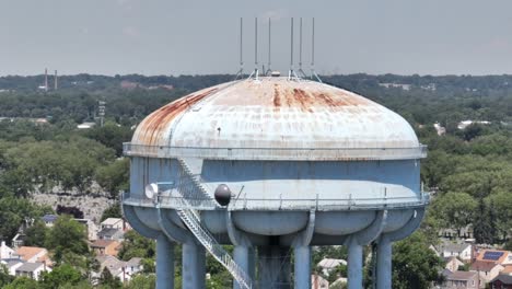 An-aerial-view-of-a-light-blue-water-tower,-rusted-from-old-age-and-weather
