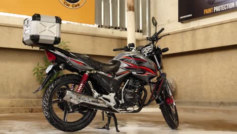 View-Of-CB150F-Motorbike-With-Storage-Box-On-Back-Resting-On-Kickstand-In-Washing-Bay-In-Karachi,-Pakistan