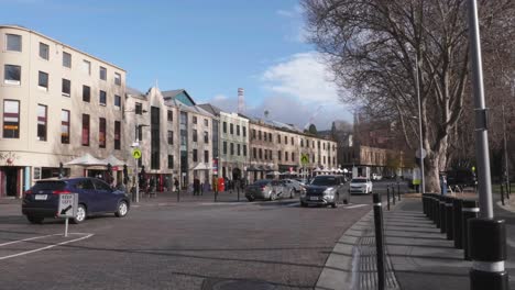 Cars-driving-along-street-with-people-walking-down-historic-street-at-Salamanca-with-architectural-buildings-on-clear-bright-winter-day,-Hobart,-Tasmania,-Australia