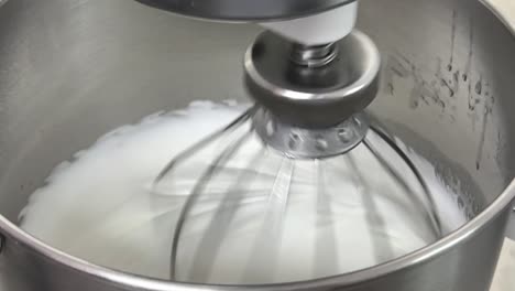 Cinematic-slow-motion-close-up-shot-of-commercial-heavy-duty-electric-mixer-mixing-and-whipping-egg-white-until-its-peak,-preparation-for-fluffy-and-airy-Swiss-meringue-buttercream