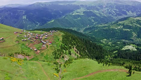Fliegen-über-Grünem-Plateau-Mit-Kleinem-Dorf-Zwischen-Bergen-Und-Steilen-Hängen