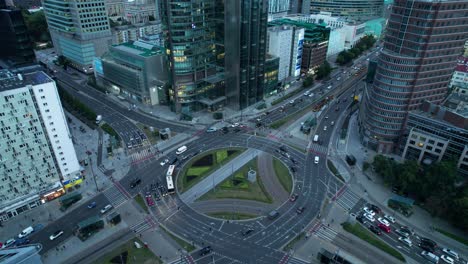 Aerial-panning-shot-of-big-traffic-roundabout-with-many-lanes-where-several-vehicles-cross-it-at-dusk-in-Rondo-ONZ,-Warsaw,-Poland