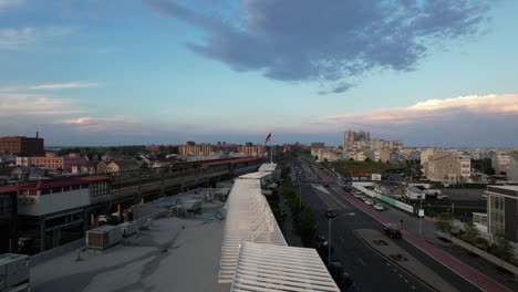 An-aerial-view-over-a-strip-mall-roof-between-an-elevated-train-station-and-a-wide-empty-road