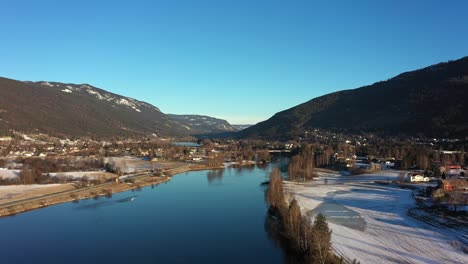 Ascending-aerial-from-Hallingdalselve-river-to-full-panoramic-view-of-Nesbyen-town-during-winter-morning-sunrise---Norway