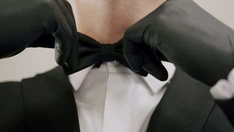 Close-up-of-the-neck-of-a-young-man-in-black-suit-adjusting-his-bow-tie-with-gloves