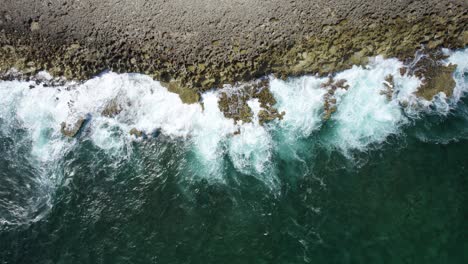 Aerial-top-down-shot-of-the-ocean-waves-crashing-on-the-rocky-shore-of-Curacao