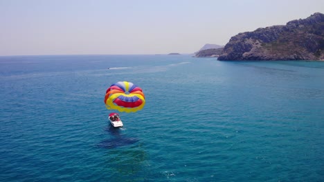 Colorful-Parachute-Pulled-By-A-Small-Boat-With-Tourists-Riding-In-The-Sea