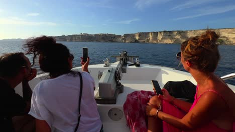 Sailing-boat-with-tourists-taking-pictures-on-board-navigates-toward-Bonifacio-cliffs-in-Corsica