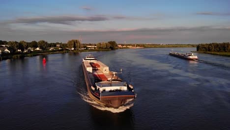 Luftaufnahme-Des-Vorderen-Bogens-Des-Fps-Waal-Frachtcontainerschiffs,-Das-Auf-Der-Oude-Maas-Fährt-Und-Während-Der-Goldenen-Stunde-An-Einem-Anderen-Schiff-Vorbeifährt