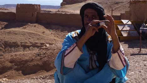 4K-Aufnahmen-Des-Marokkanischen-Kobra-Zauberers,-Der-Mit-Seiner-Kobra-In-Der-Nähe-Von-Kasbah-Ait-Ben-Haddou-Im-Atlasgebirge-Von-Marokko-Auf-Der-Straße-Sitzt