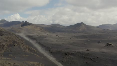 Ascending-drone-shot-showing-van-driving-on-dusty-road-between-black-sand-desert-and-volcanoes---Iceland-Tour,Europe