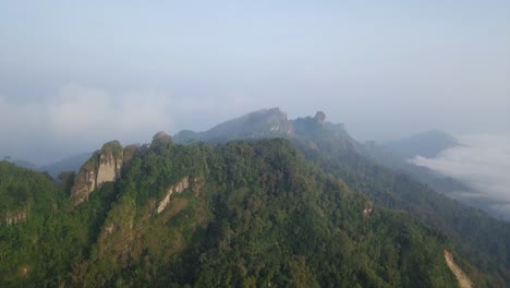 Drohne-Rückwärtsflug-Zeigt-Bergkette-Mit-Grünen-Pflanzen-Auf-Berggipfel-Bedeckt-Von-Nebel-Und-Wolken---Menoreh-Hügel,-Indonesien