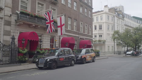 Black-taxi-cab-and-British-flags-on-a-street-in-Mayfair,-London