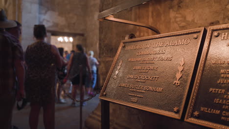 The-Heroes-of-the-Alamo-plaque-featuring-James-Bowie-and-David-Crockett-inside-the-Alamo-with-tourists-in-the-background