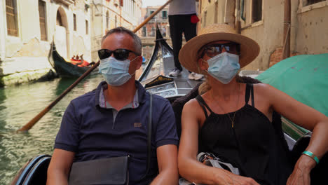Pareja-De-Turistas-Con-Máscaras-Y-Gafas-De-Sol-Recorriendo-Una-Góndola-En-El-Gran-Canal-De-Venecia,-Italia
