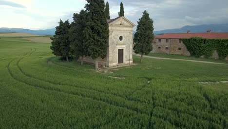 [Aerial-footage]-Rising-above-wheat-field-pointing-to-Vitaleta-Chapel-in-Tuscany,-Italy