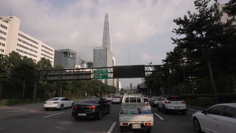 Cars-stuck-in-traffic-jam-at-Songpa-daero-freeway-with-a-view-of-Lotte-World-Tower-at-sunset,-Dirver's-POV