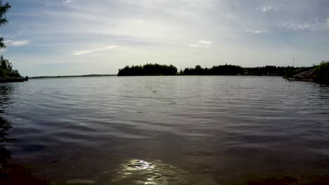 Lakeshore-boreal-forest-time-lapse-low-shot-zoom-out-on-sand-beach-of-waves,-boats-and-clouds-in-Point-du-Bois-Manitoba-Canada-Whiteshell-provincial-park-in-the-Great-Canadian-shield