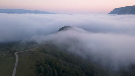 Aerial-footage-showing-a-hill-surrounded-by-a-valley-covered-in-fog