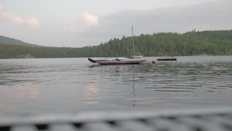 Barco-Flotando-En-Un-Lago,-Filmado-Desde-La-Esquina-De-Un-Muelle