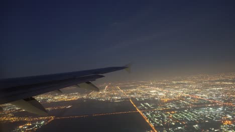 Avión-Volando-Sobre-Una-Ciudad-Brillante-Por-La-Noche-Al-Despegar