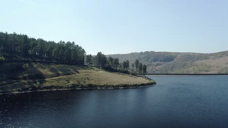 Aerial-shot-over-Kinder-Reservoir-water-showing-tall-trees-on-the-perimeter-and-some-of-the-Dam-Wall