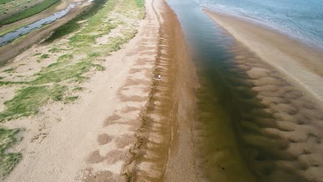 Overhead-Drone-shot-following-a-runner-along-the-beach-in-Holme-next-the-Sea,-Norfolk,-England