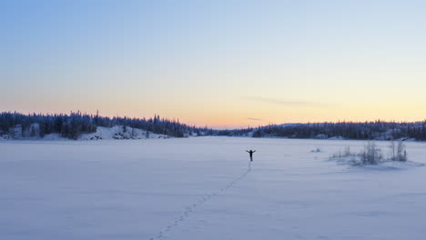 Aerial-of-One-man-walking-on-frozen-lake-in-wilderness-at-dawn,-canada
