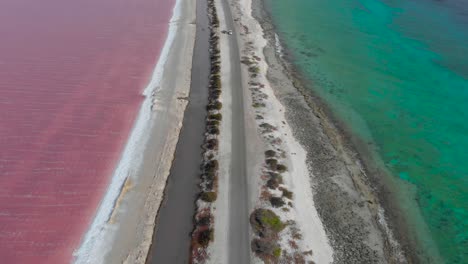 Aerial-reveal-view-of-the-pink-salt-flats-of-Bonaire-contrasted-with-the-turquoise-ocean-along-the-road